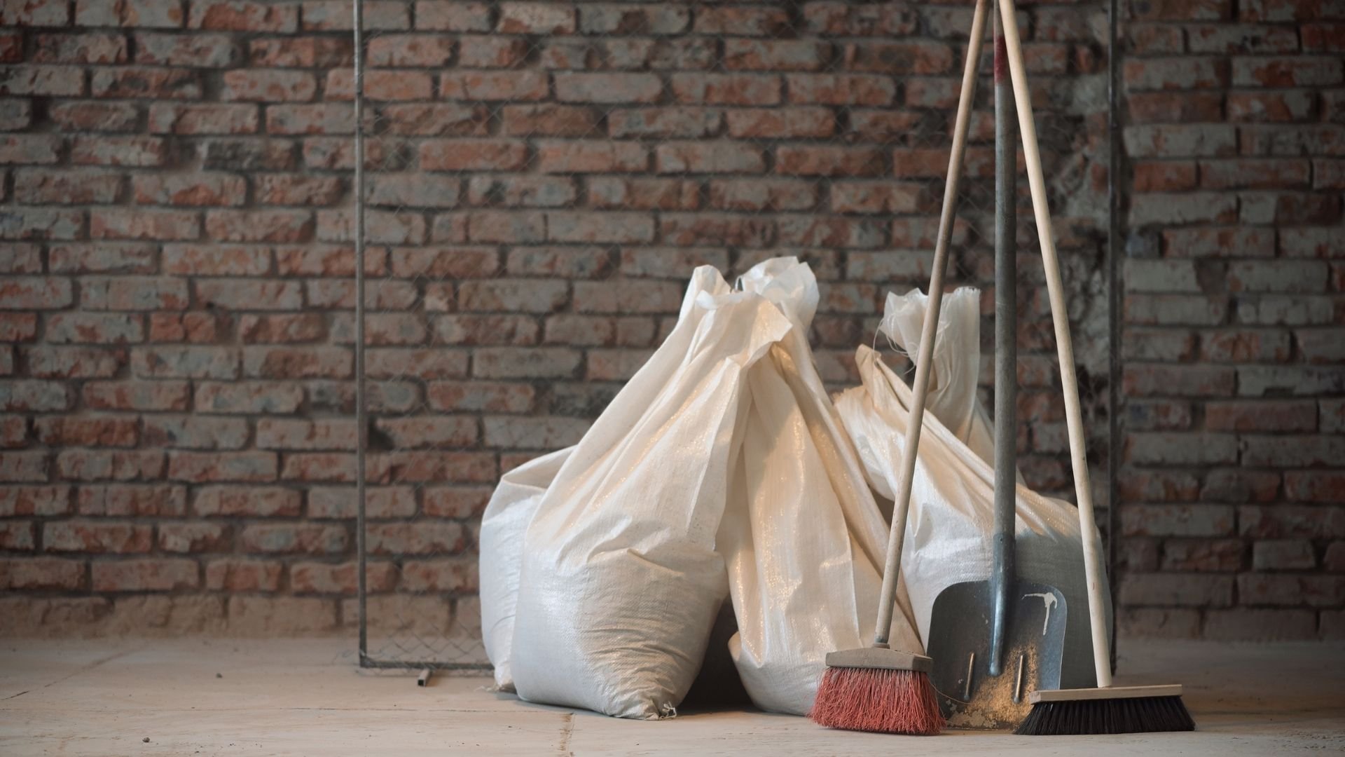 Construction site with white bags, brooms, and tools against brick wall background.