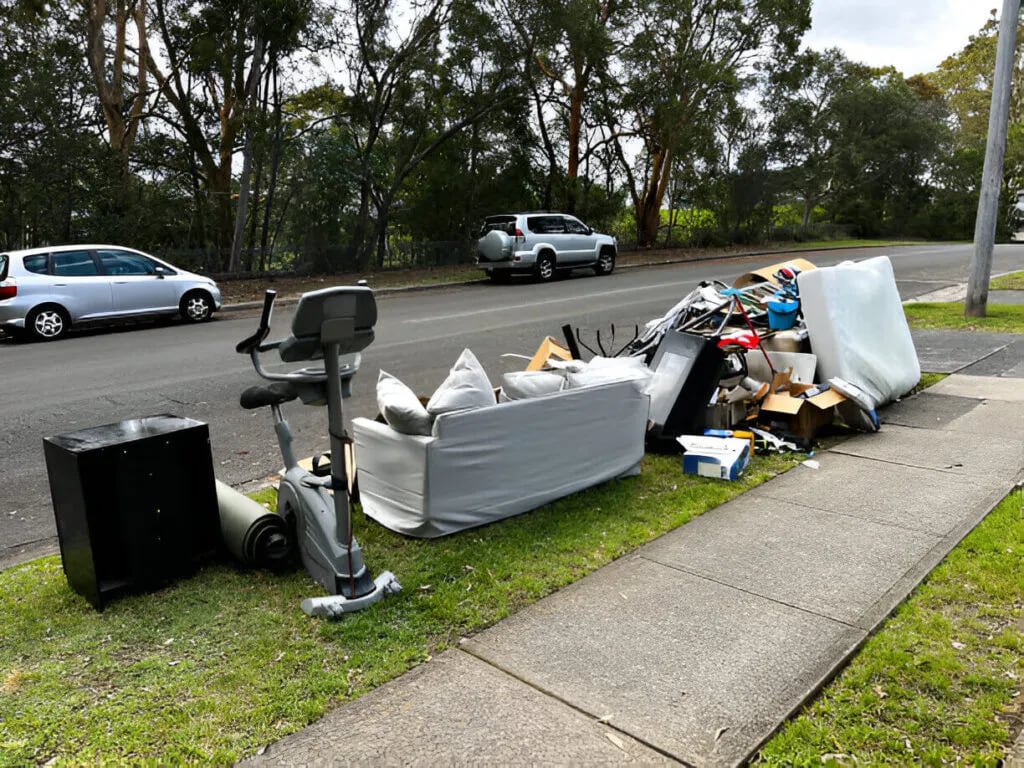 Pile of discarded furniture and items including a couch and exercise bike on suburban street