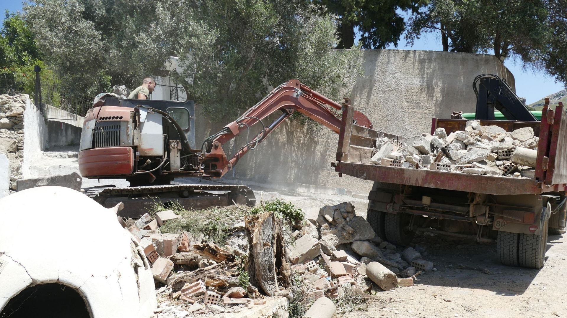 Excavator loading construction debris and rubble onto a truck at demolition site