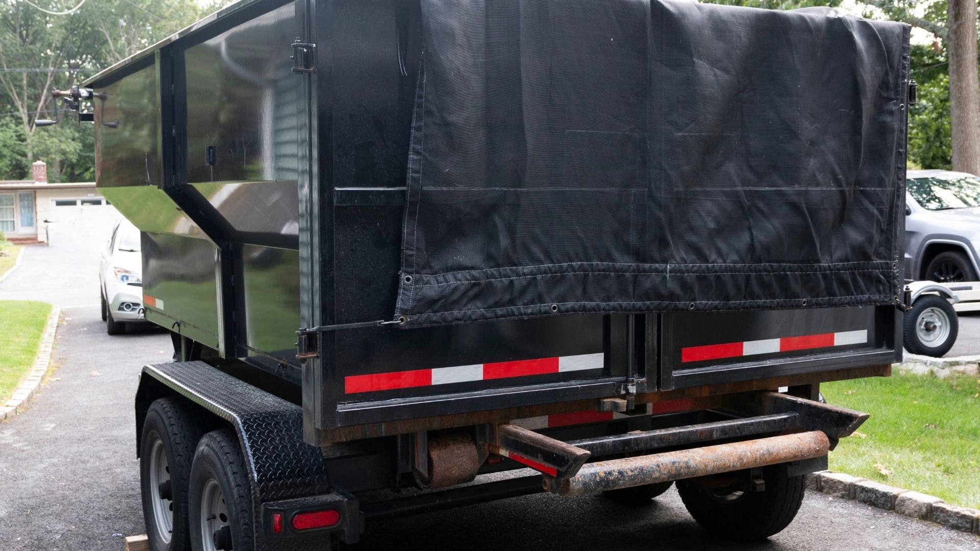 Black enclosed trailer with red and white reflective stripes parked in driveway.